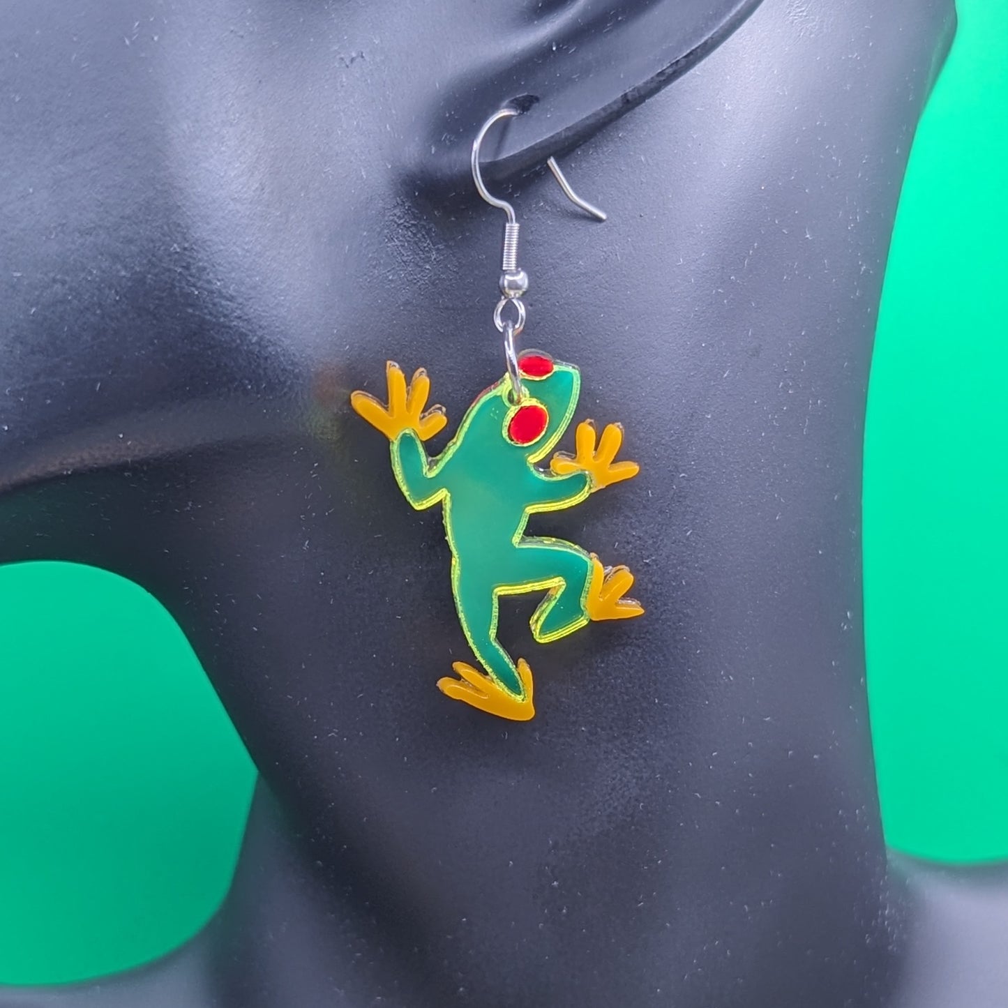 Neon green tree frog earrings with red eyes and orange feet on a model ear.
