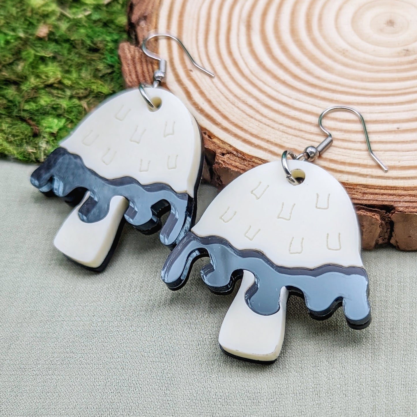 Inky cap mushroom earrings made with beige and dark gray acrylics on stainless steel fishhooks on a wood slice