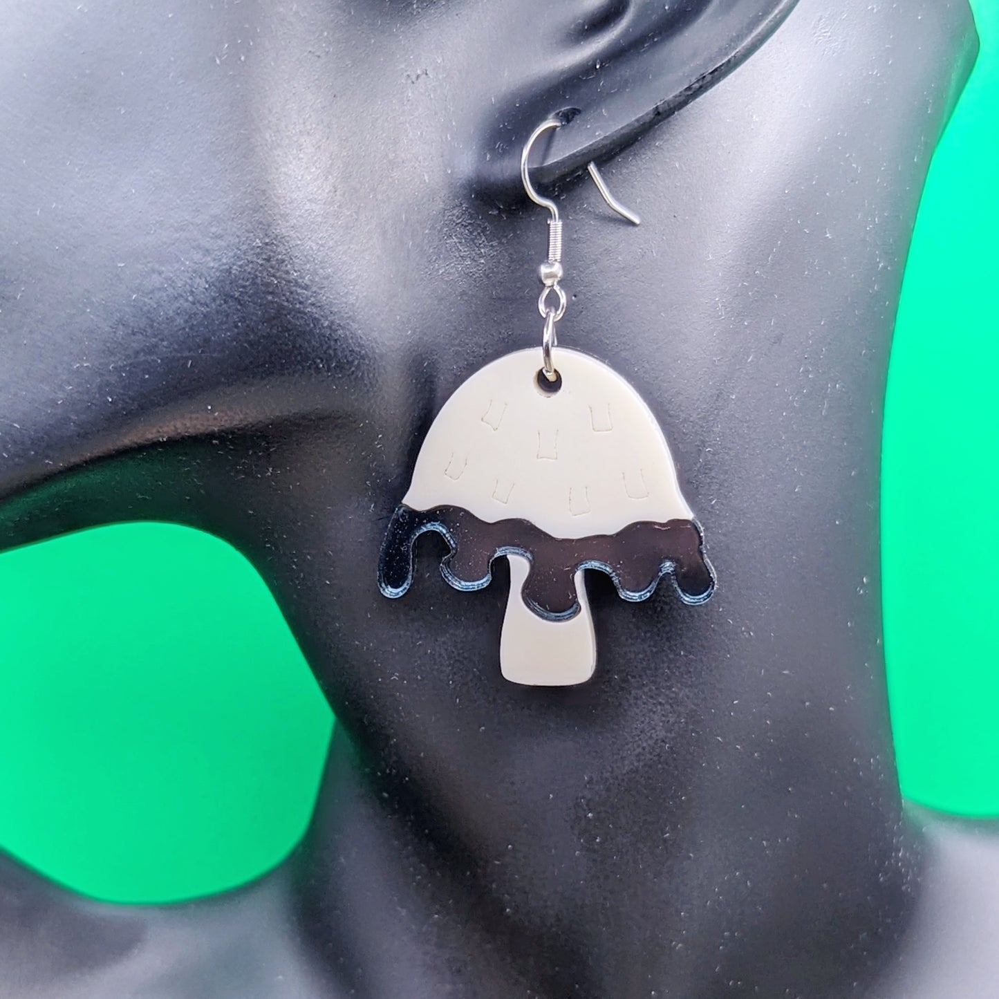 Inky cap mushroom earrings made with beige and dark gray acrylics on stainless steel fishhooks on a model ear.