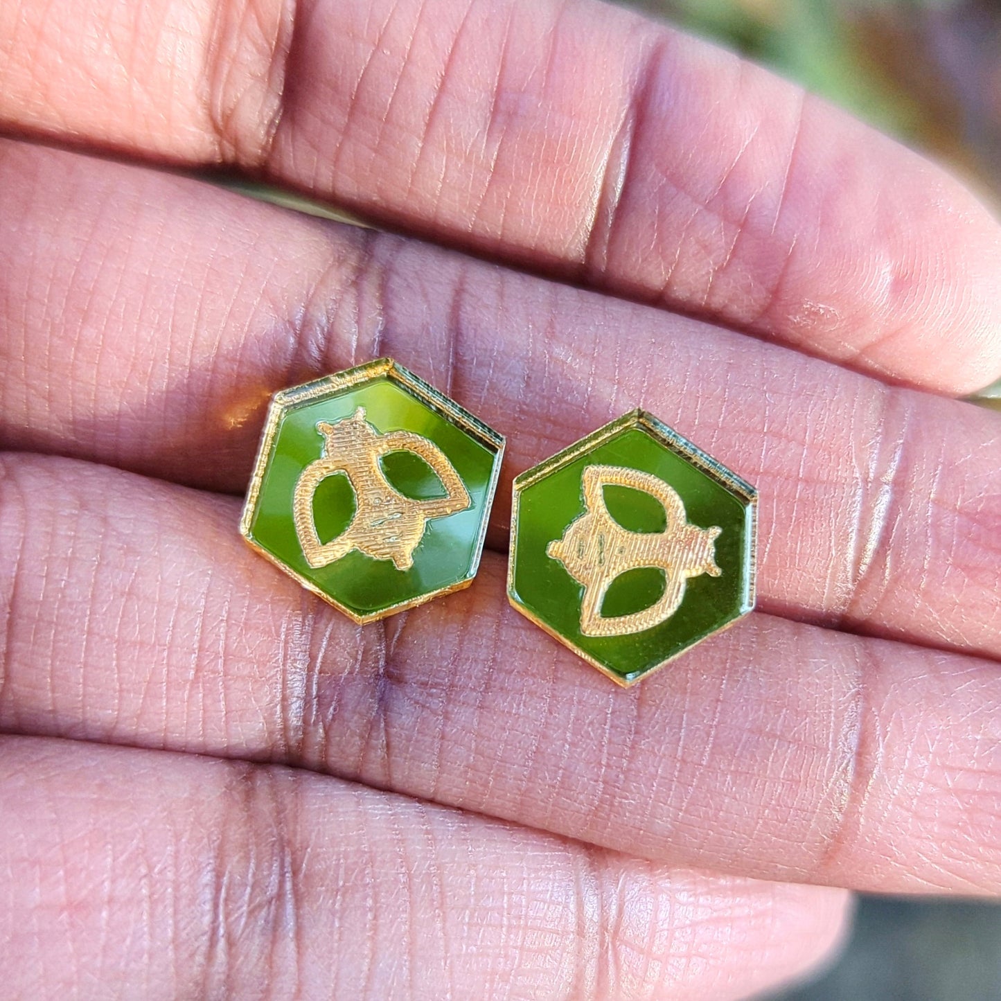 Hexagon shaped stud earrings in pale gold with engraved bees in hand for scale.