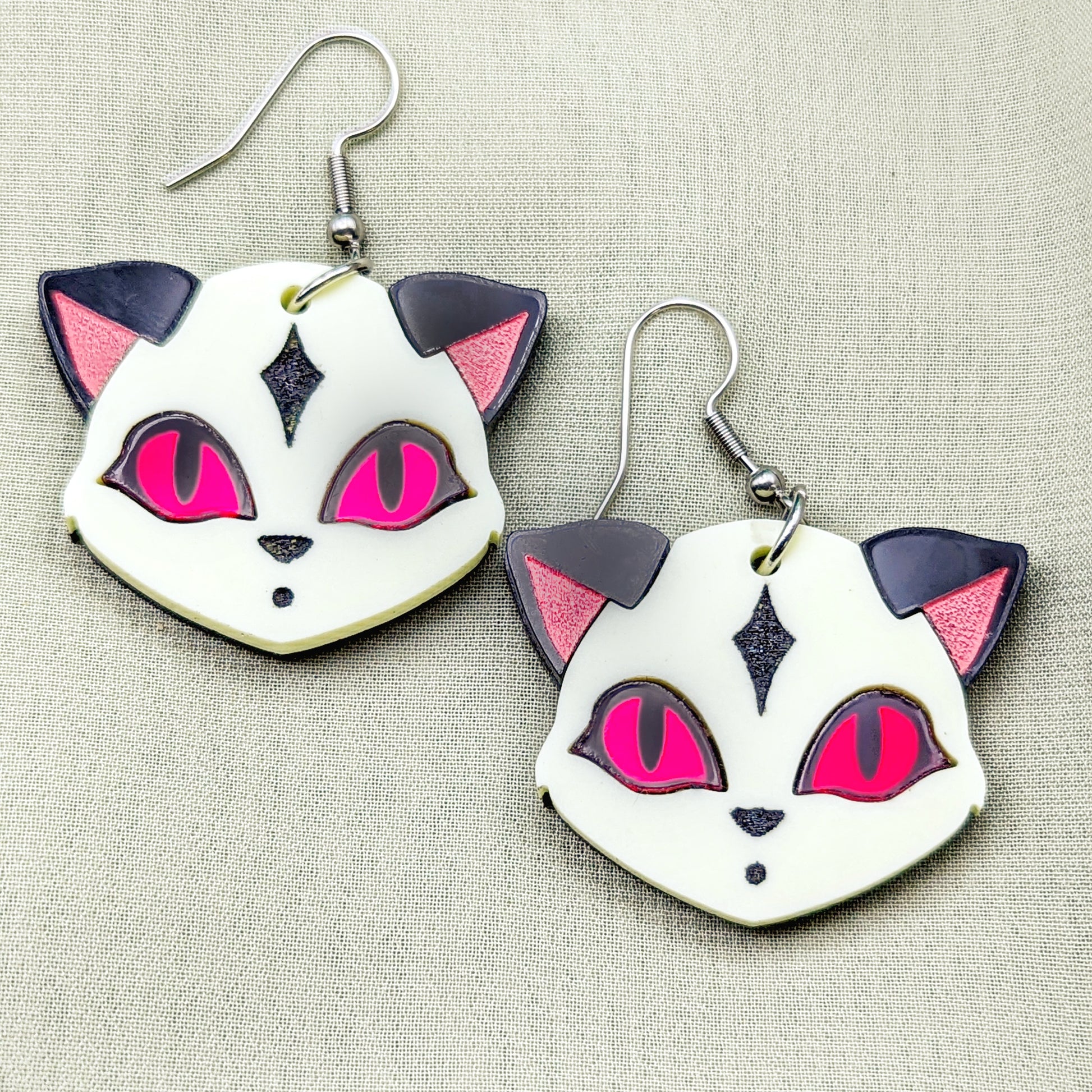 Pastel yellow fox face earrings with black ears, red eyes, and engraved details.