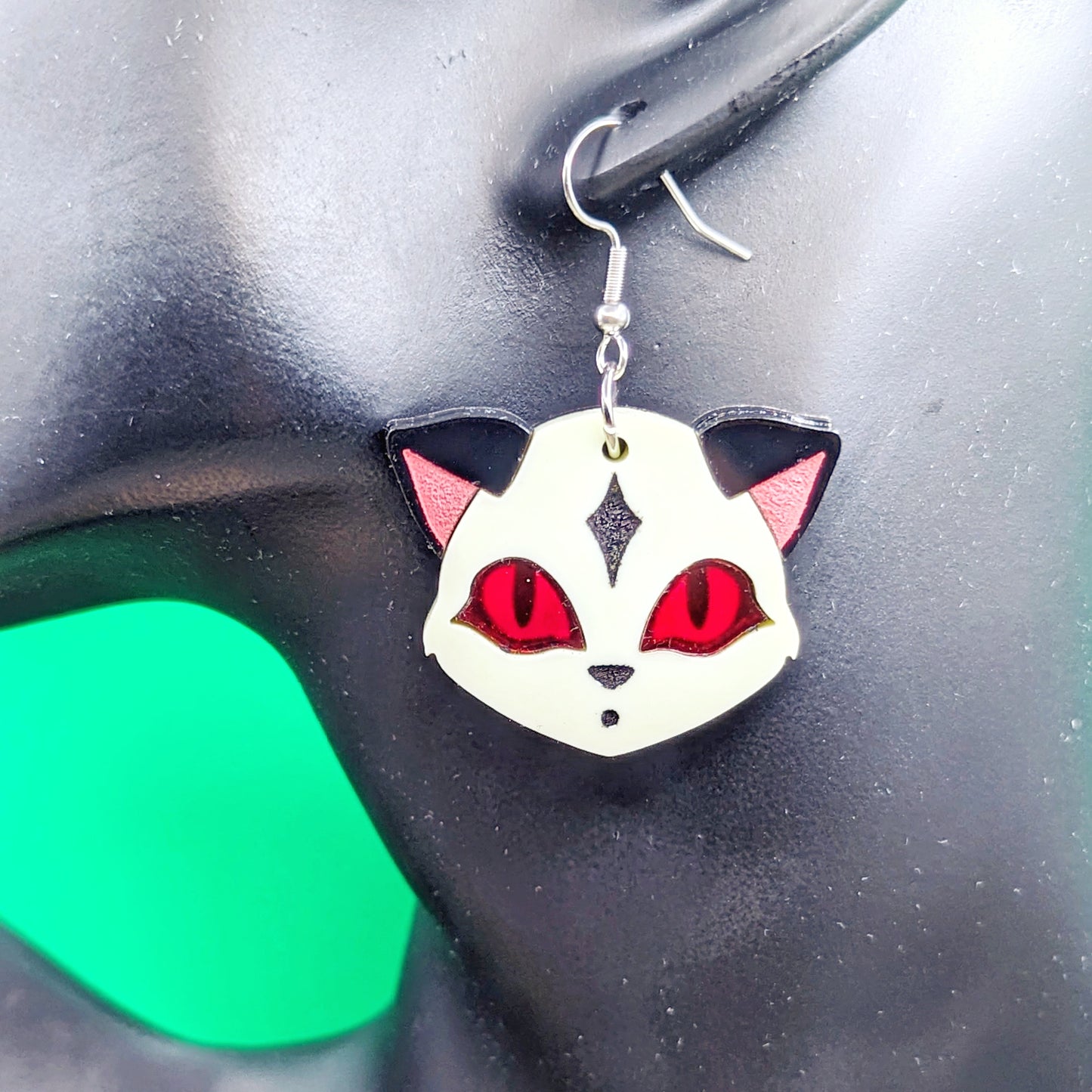 Pastel yellow fox face earrings with black ears, red eyes, and engraved details on a model ear.