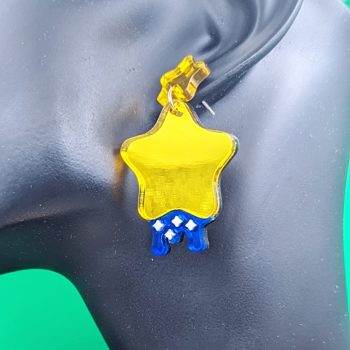 yellow star shaped dangle earrings with blue dripping below and small pastel yellow stars with yellow star stud posts hanging from a model ear for scale