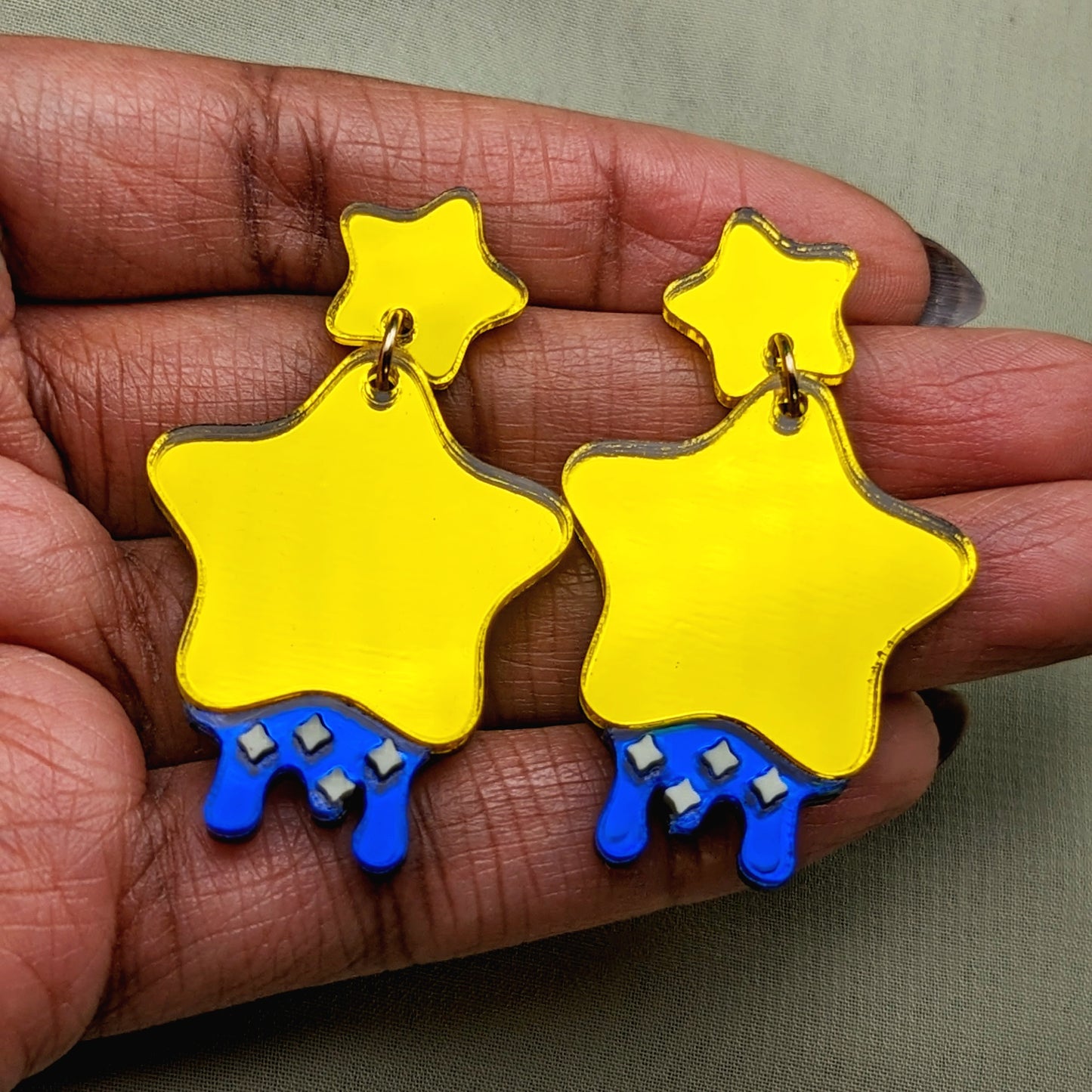 yellow star shaped dangle earrings with blue dripping below and small pastel yellow stars with yellow star stud posts in hand for scale