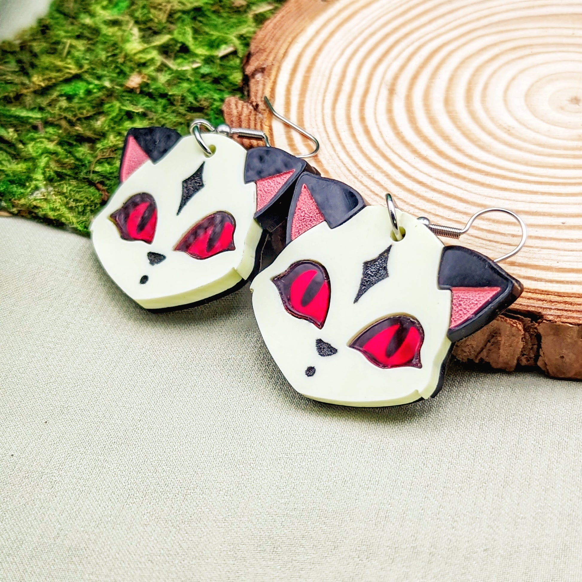 Pastel yellow fox face earrings with black ears, red eyes, and engraved details on a wood slice.