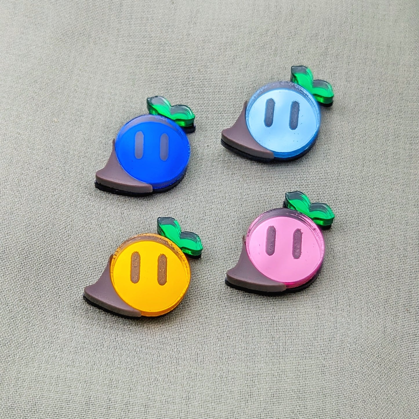 Magical seed stud earrings in dark blue, light blue, orange, and pink with green sprouts and engraved eyes