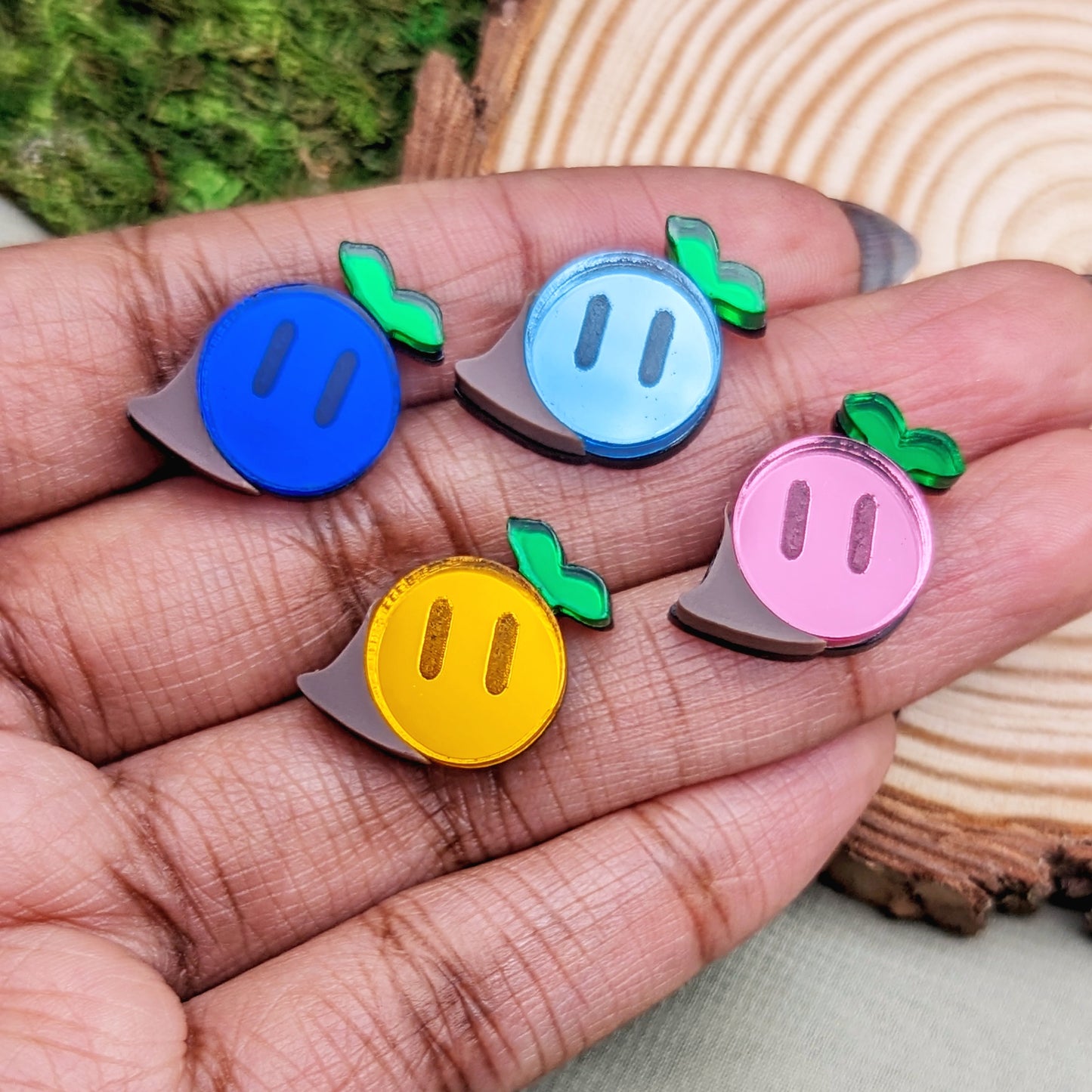 Magical seed stud earrings in dark blue, light blue, orange, and pink with green sprouts and engraved eyes in hand for scale