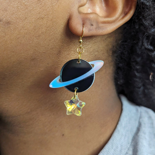 A black planet earring with an iridescent ring. An iridescent glass star bead hands from the bottom.