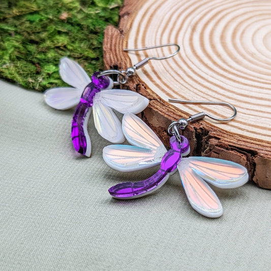 Purple dragonfly dangle earrings with matte iridescent engraved wings on a wood slice