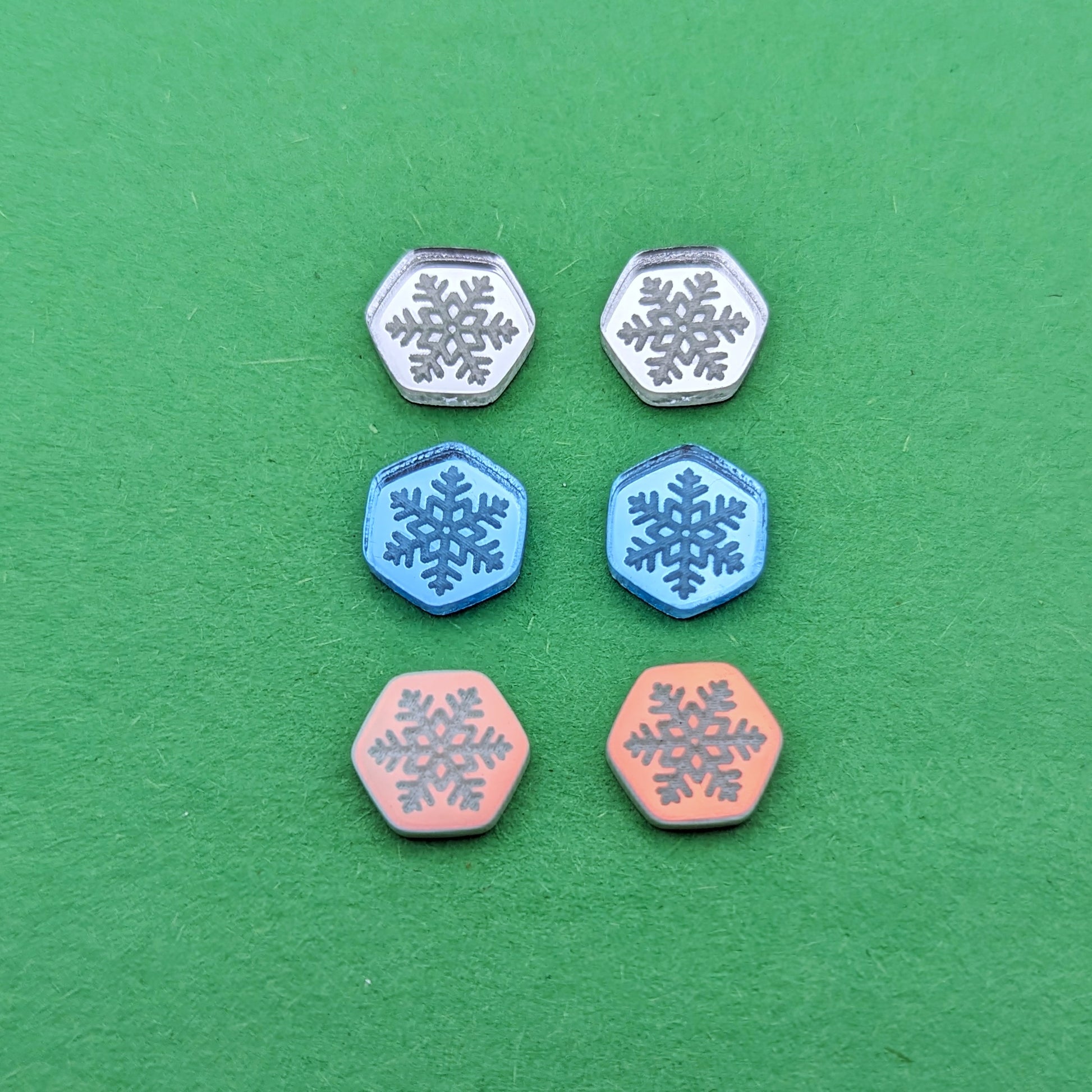 Three pairs of hexagonal stud earrings in silver, light blue, and iridescent with engraved snowflakes. 