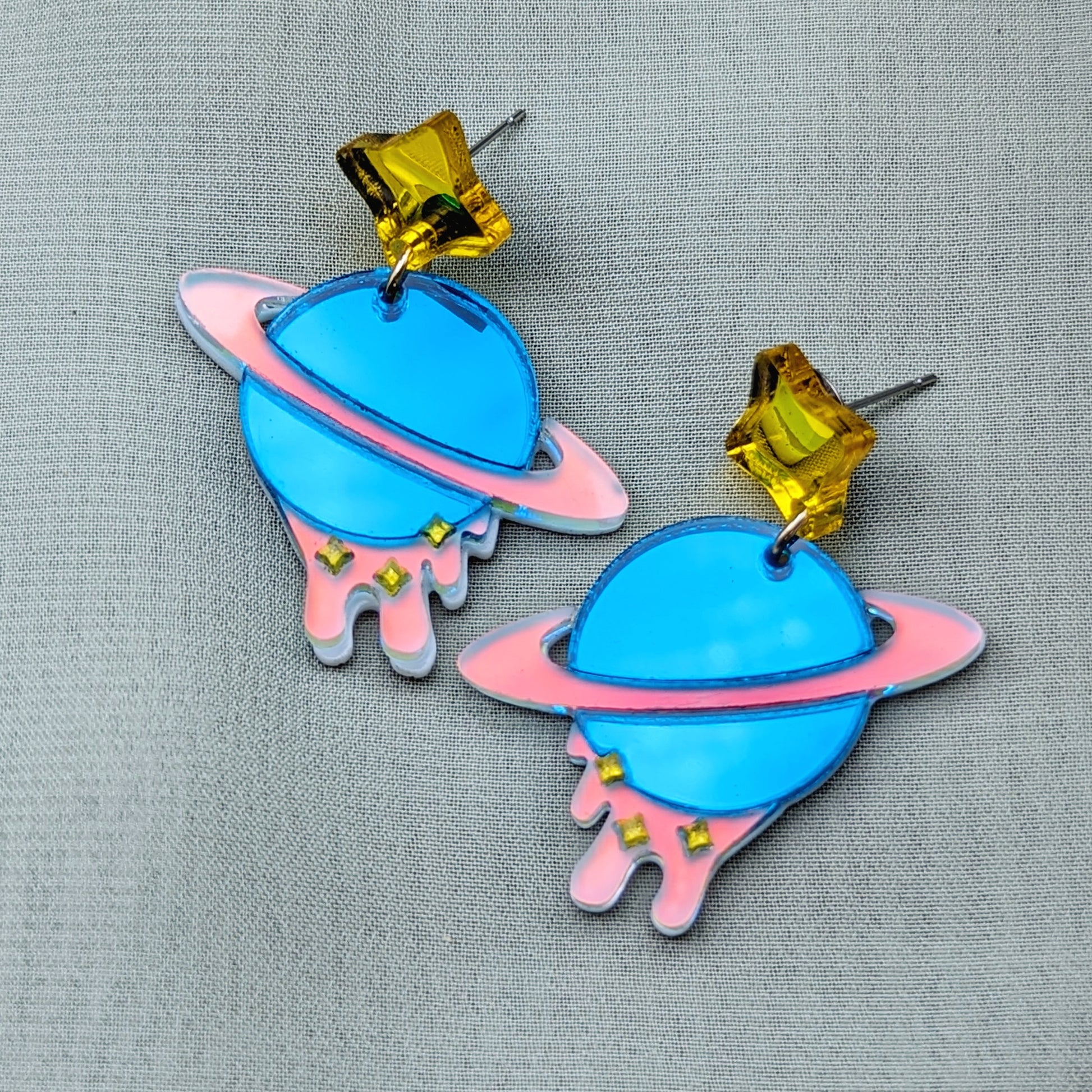 teal planet shaped dangle earrings with matte iridescent planetary rings, iridescent dripping below and small yellow stars with yellow star stud posts 