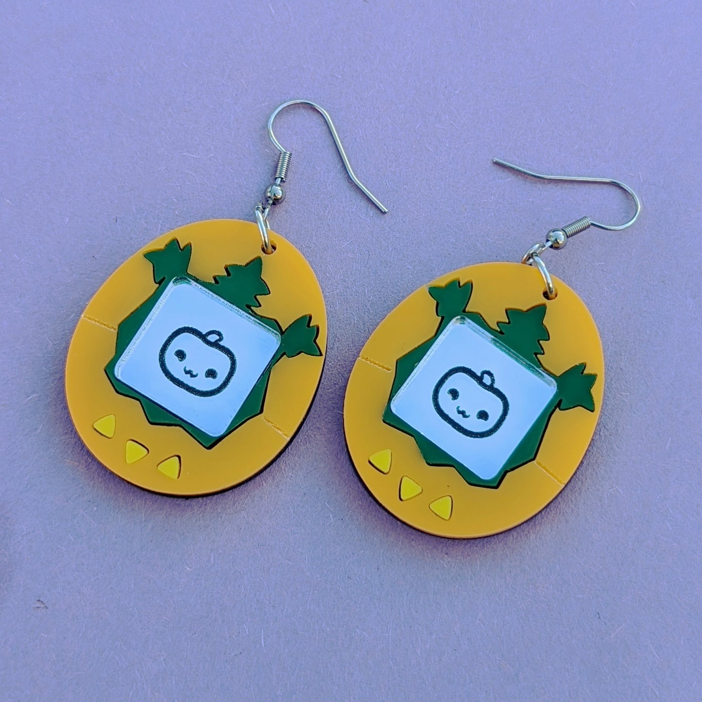 Halloween Pumpkin Tamagotchi Acrylic Earrings with Stainless Steel Ear Hooks. Orange and Green earrings with yellow triangle buttons and an engraved silver screen featuring a cute jack-o-lantern.