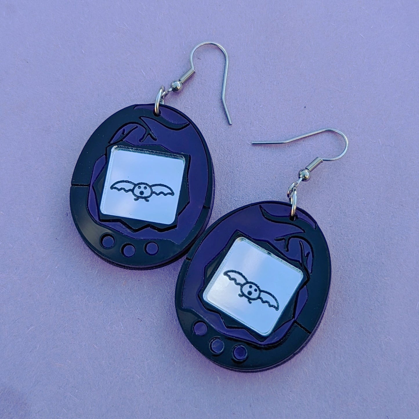 Halloween Bat Tamagotchi Acrylic Earrings with Stainless Steel Ear Hooks. Purple and Black earrings with an engraved silver screen featuring a bat.