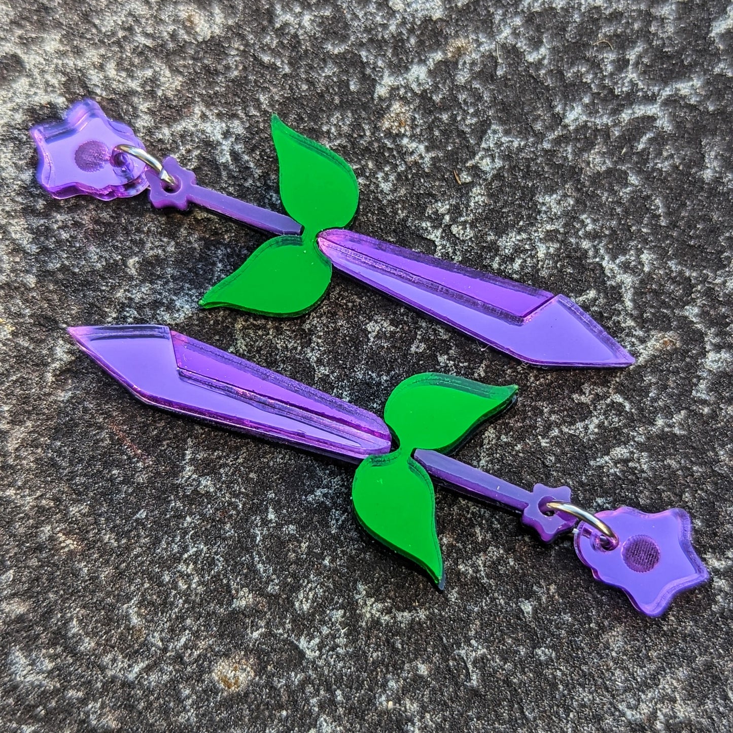 stardrop themed sword earrings. purple two-toned blades with green leaf hilts, a purple hand with a star at the end.