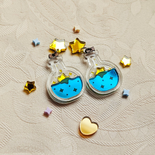 Star potion bottle earrings made with clear acrylic with shiny teal for the liquid and yellow for the stars. A wooden cork is at the top and they hang from shiny yellow star stud posts.